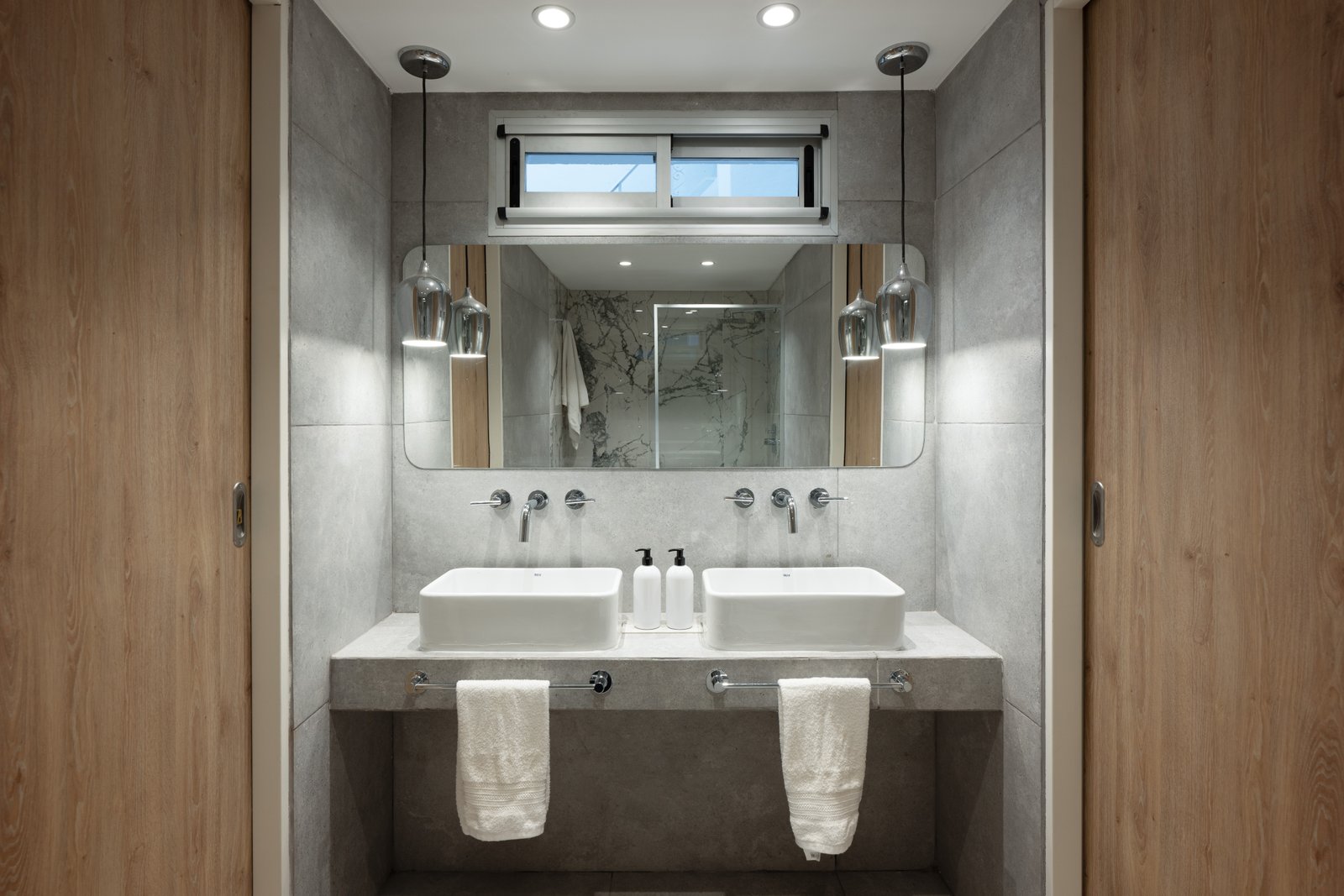 Baño moderno con dos bachas de mármol, espejos amplios y luz indirecta — proyecto Casa Gainza, por Estudio Plats, en Caballito